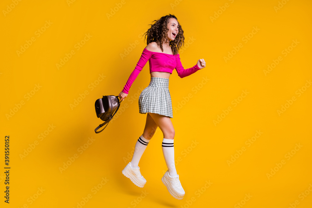 Full length profile photo of lady curly hairdo open mouth bag jump wear pink cropped top unclothed shoulders mini skirt white sneakers isolated yellow color background Full length profile photo of lady curly hairdo open mouth bag jump wear pink cropped top unclothed shoulders mini skirt white sneakers isolated yellow color background