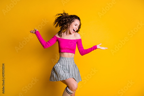 Photo portrait of carefree woman standing on one leg hands to sides wearing pink crop-top checkered mini skirt long socks isolated on vivid yellow colored background