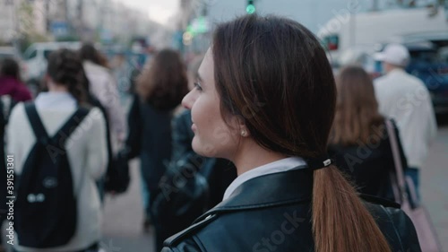 Back view of young stylish woman in a leather jacket walking in the downtown, in crossing the road through the crowd. Footage of blurred people coming in downtown from the back, busy city life 4k