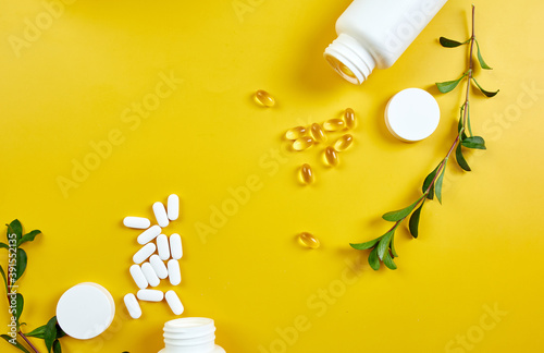 Flat lay of pills, fish oil, vitamins with green leavws on yellow background, Healthcare concept, healthy food, supplements for healthy good life, Immune booster.. photo