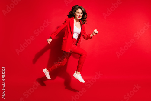 Full length profile photo of pretty young lady run move toothy smiling wear jacket trousers sneakers isolated red color background
