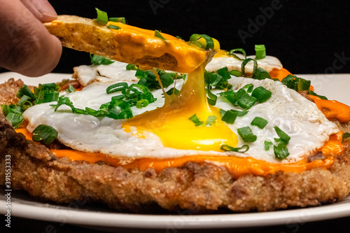 Papa frita rompiendo un huevo frito sobre una milanesa  photo