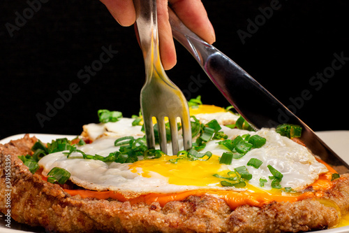 Foto Plano detalle de manos cortando huevo frito sobre milanesa
