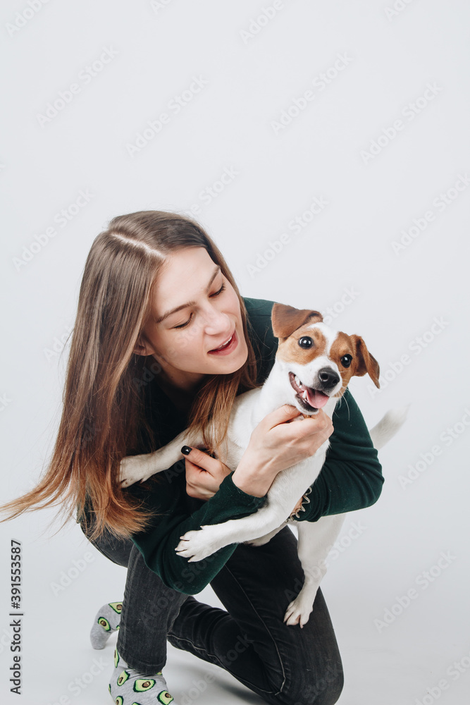 Young white woman hugs her jack russell terier puppy. Isolated on white background. Studio portrait in action. Owner and her dog posing together. Young white woman hugs her jack russell terier puppy. Isolated on white background. Studio portrait in action. Owner and her dog posing together.