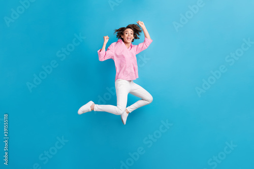 Full size photo of ecstatic girl jump raise fists wear formal clothes sneakers isolated over blue color background