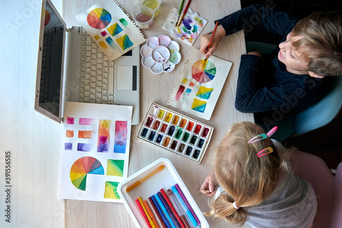 Children painting pictures with watercolor paints during art lesson. Pupils are concentrating on drawing with brush. Watercolor color wheel and palette. Color theory beginner hobby lessons