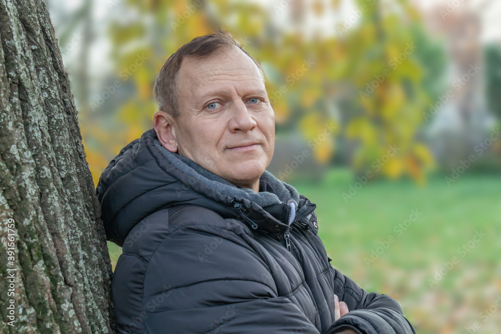 portrait of a fifty-year-old man leaning against a tree against the background of an autumn landscape portrait of a fifty-year-old man leaning against a tree against the background of an autumn landscape