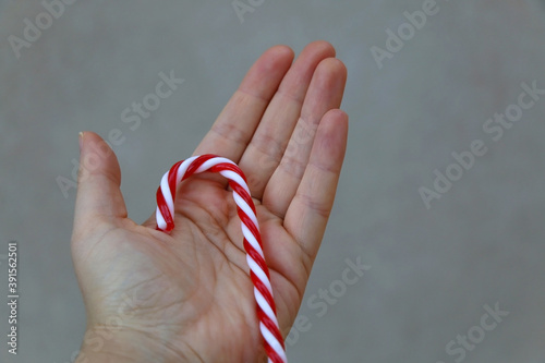 Unrecognizable person holding a candy cane decoration. Selective focus, simple background.