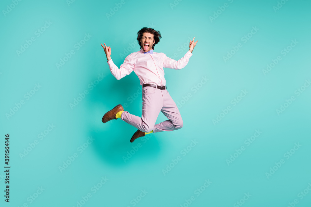 Full length photo of cool crazy guy jump show horns fingers stick tongue isolated on turquoise color background Full length photo of cool crazy guy jump show horns fingers stick tongue isolated on turquoise color background