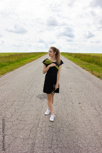 A girl in a black dress on the road with wheat in her hands.