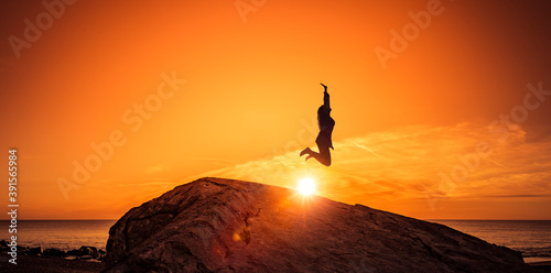 Frau hüpft von einem Felsen bei Sonnenuntergang am Strand