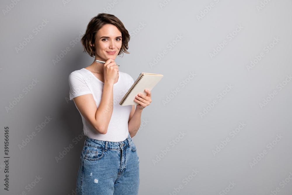 Photo of young attractive cheerful positive woman hold notebook diary write hand touch chin isolated over grey color background Photo of young attractive cheerful positive woman hold notebook diary write hand touch chin isolated over grey color background