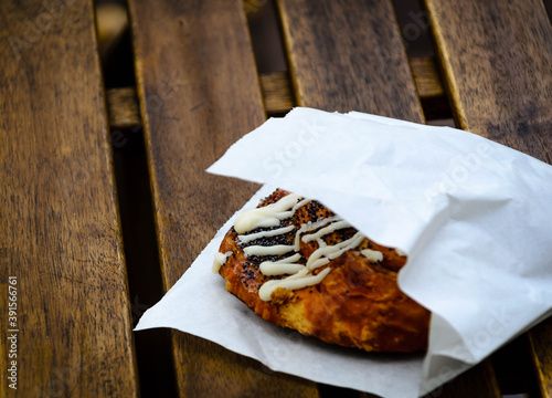 A bun with poppy in a paper bag on the table of a street cafe-public food.