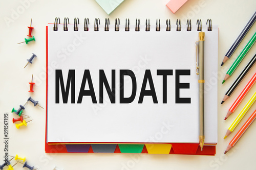 the word mandate written in a notebook on a white background with pencils. concept of human right to anything