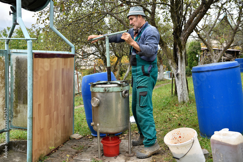Obraz na płótnie The fruit farmer rotates the press by hand while pressing the apples into fruit must w salonie