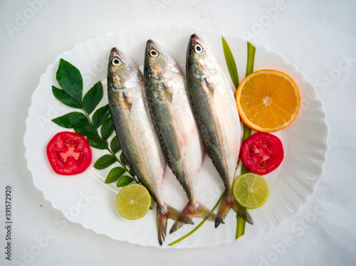 Fresh Indian Mackerel Fish Decorated with herbs and Vegetables on a white plate. photo