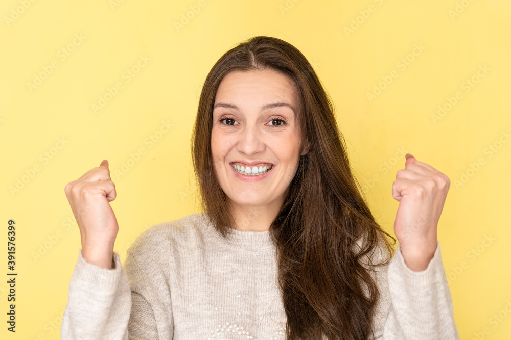 Joyful tatar young brunette woman dressed casually clenching fists and smiling, celebrating victory isolated in yellow studio Joyful tatar young brunette woman dressed casually clenching fists and smiling, celebrating victory isolated in yellow studio