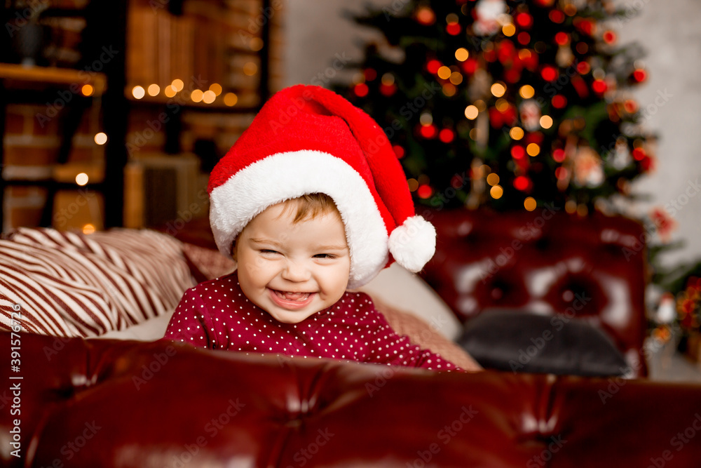 Cute baby Santa sits at home near the Christmas tree with gifts Cute baby Santa sits at home near the Christmas tree with gifts