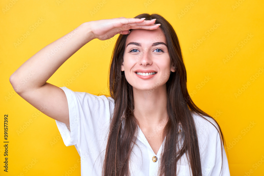 Portrait of young brunette woman dressed in a white casual looking far away with hand over head and a happy smile. Searching concept isolated on yellow background in studio Portrait of young brunette woman dressed in a white casual looking far away with hand over head and a happy smile. Searching concept isolated on yellow background in studio