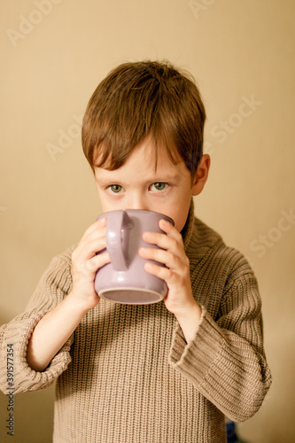 boy drinks cocoa. Warm autumn photography. A boy in a brown sweater drinks from a mug.