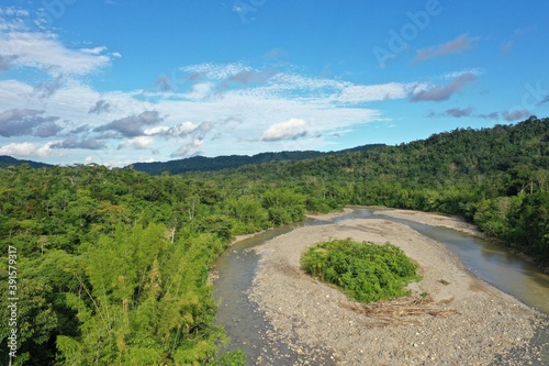 Aerial view of a small river in a tropical rainforest with driftwood in the middle of the river and a stunning cloudscape