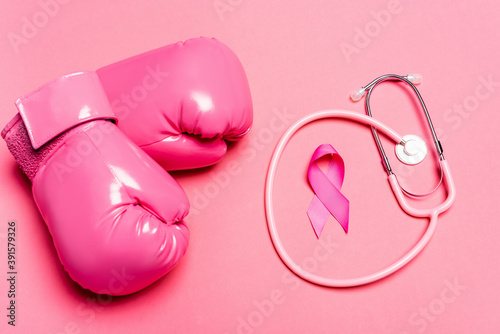 Top view of boxing gloves, symbol of breast cancer awareness and stethoscope on pink background