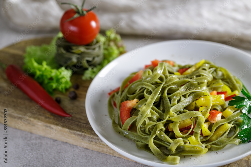 Boiled spinach tagliatelle seasoned with spices and vegetables on wooden board