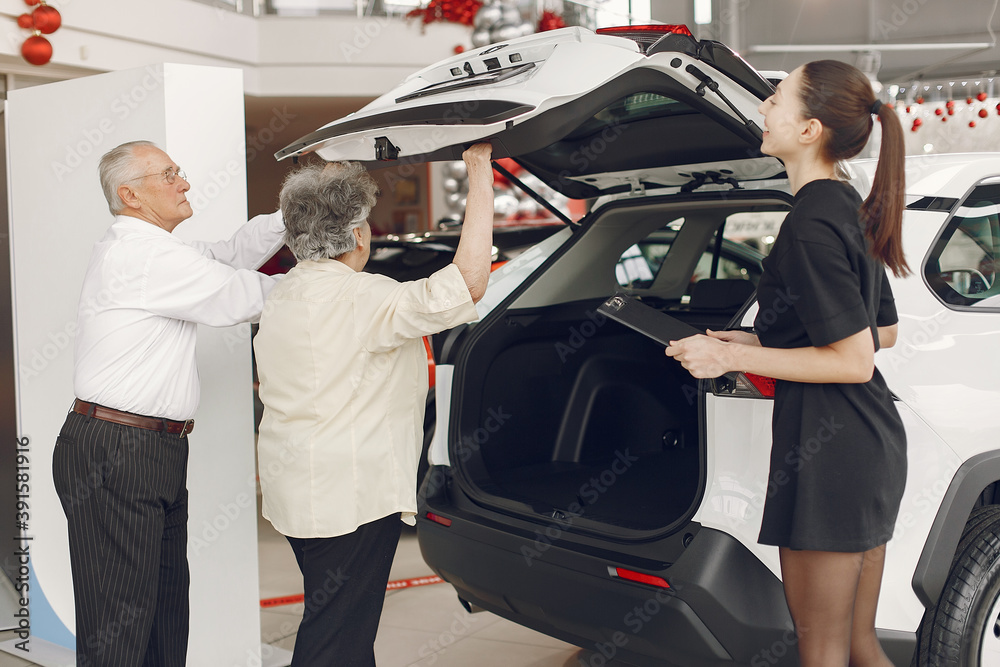 Senior in a car salon. Old couple buying the car. Elegant woman helps a old people buy a car.