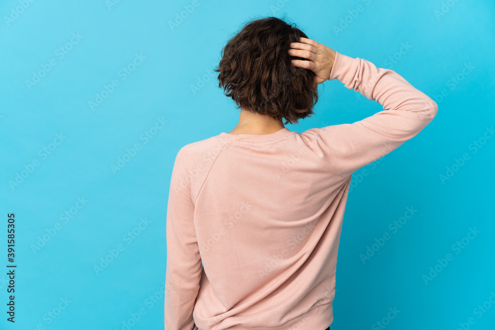 Young English woman isolated on blue background in back position and thinking Young English woman isolated on blue background in back position and thinking