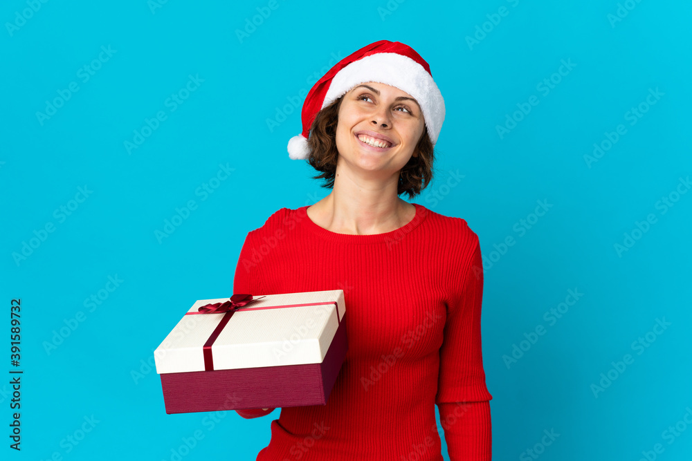 English girl with christmas hat holding a present isolated on blue background thinking an idea while looking up English girl with christmas hat holding a present isolated on blue background thinking an idea while looking up