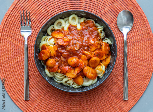 Dischi pasta with sausage, onion and balognese sauce in a black plate on red background. Copy space, No focus, specifically. photo