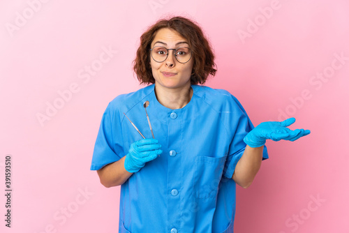 Woman English dentist holding tools over isolated on pink background having doubts while raising hands
