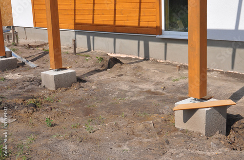 Close-up of wooden posts, structural beams anchored to concrete footing with bolts to support a patio roof of the house under construction. photo