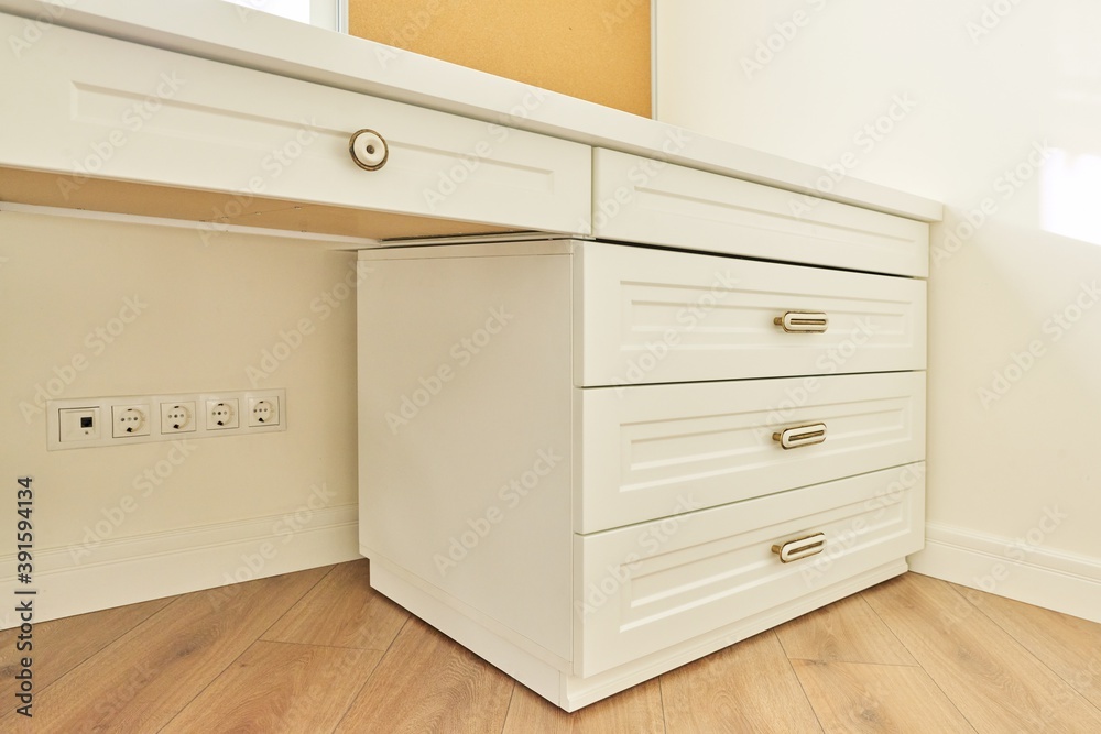 Fototapeta premium White wooden chest of drawers with vintage bronze handles under desk