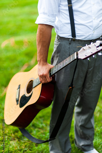 Man holding a guitar in a green field.
