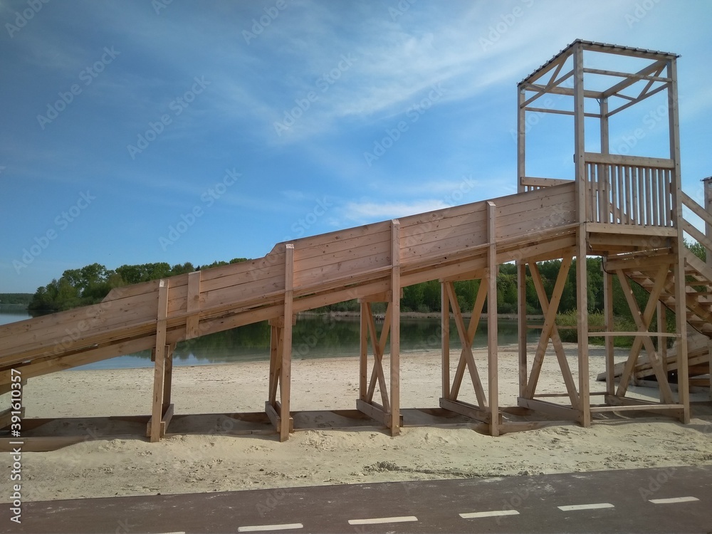 new wooden slide by the lake of the river on the background of sand and water in summer
park in Solnechnogorsk, Lake Senezh