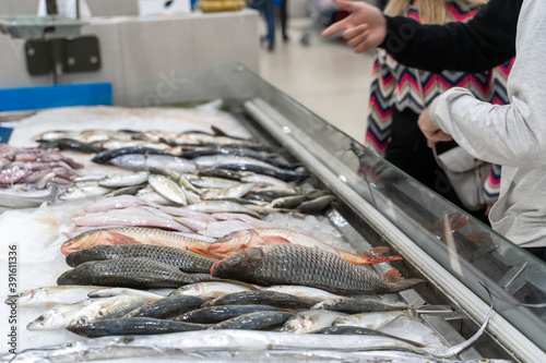Adult buyers searching for fresh seafoods on crushed ice in open display of fish shop. Woman choosing frozen food from a supermarket freezer.