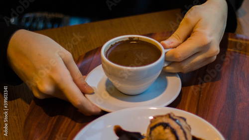 Hands holding a cup of Turkish coffee served on a wooden table with an ice-cream. 
