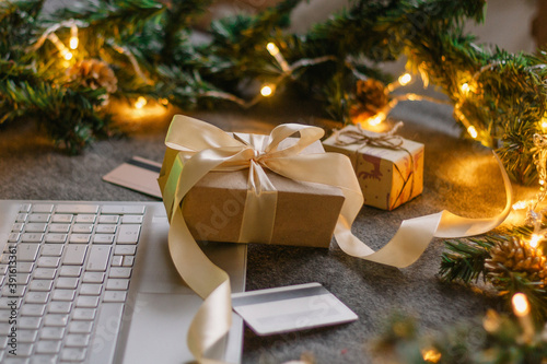 Christmas shopping online with a credit card for the holiday. Laptop with gifts on the table next to fir branches and a garland of lights © Anastasiya Famina