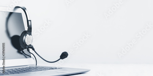 Laptop. Mockup screen and headphones on grey desk and plain background banner. Distant learning or working from home, online courses or support minimal concept. Helpdesk or call center headset photo