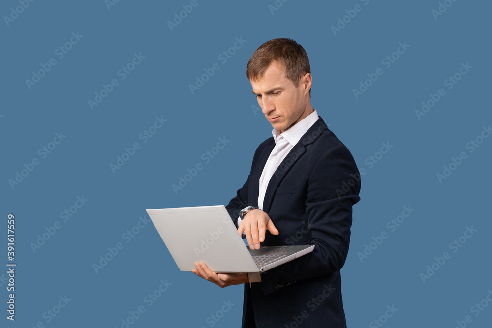 A man businessman in a business suit looks at a laptop on the weight in his hands. Studio shot concept about remote work without office on blue background.