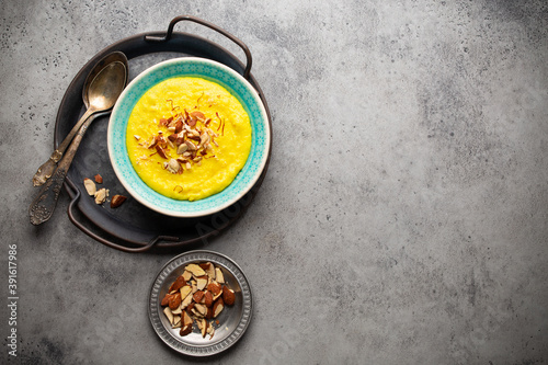 Traditional Indian dish Kheer, rice milk pudding with almonds and saffron in blue ceramic bowl with spoons on stone rustic background, top view. Dessert meal of Indian cuisine, space for text