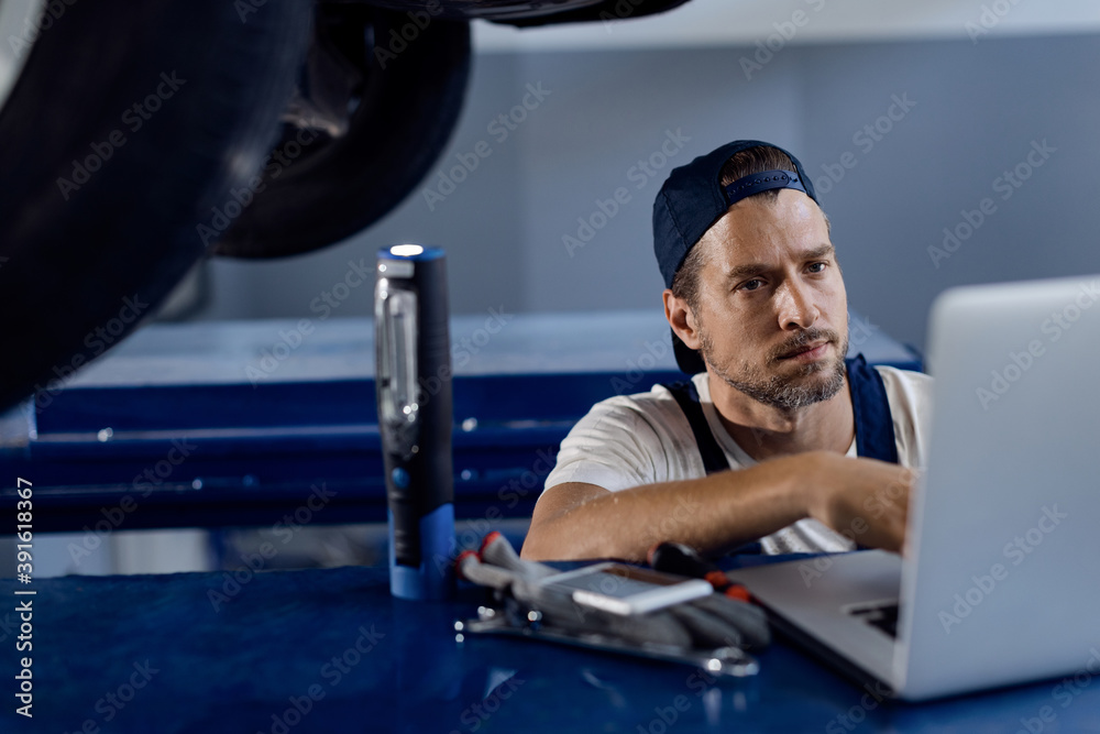 Car mechanic working on laptop at auto repair shop.