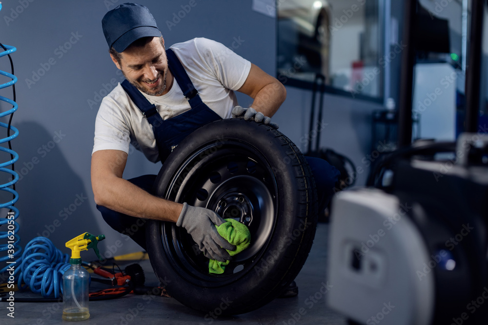 Happy car mechanic cleaning a tire while working in repair shop. Happy car mechanic cleaning a tire while working in repair shop.