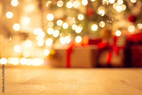 Blurred view of christmas tree in bright warm lights and beautiful presents under it, focus on the floor. Festive atmosphere, new year holidays background.