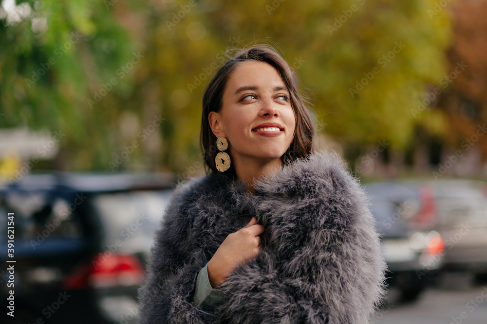 Outdoor portrait of stylish pretty woman with golden earnings walking on the street on city background