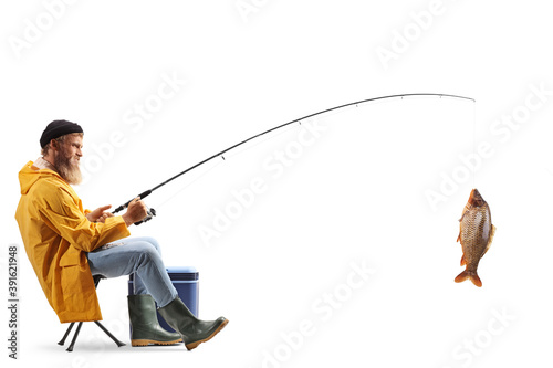Fotografia, Obraz Full length profile shot of a young fisherman sitting on a chair and catching fi