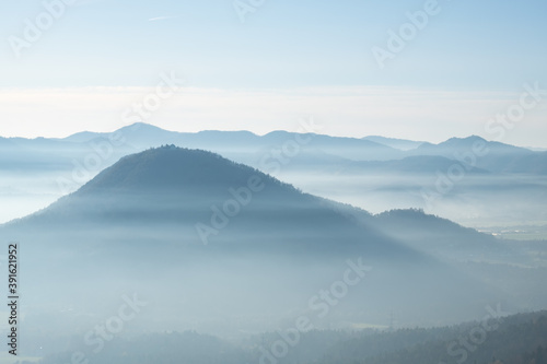 mystical and romantic mountain scenery with hilltops softly peaking out of white clouds. Fog flowing through the valleys. Layers of mountains in a beautiful landscape with the alps in the background  © RoMaLi