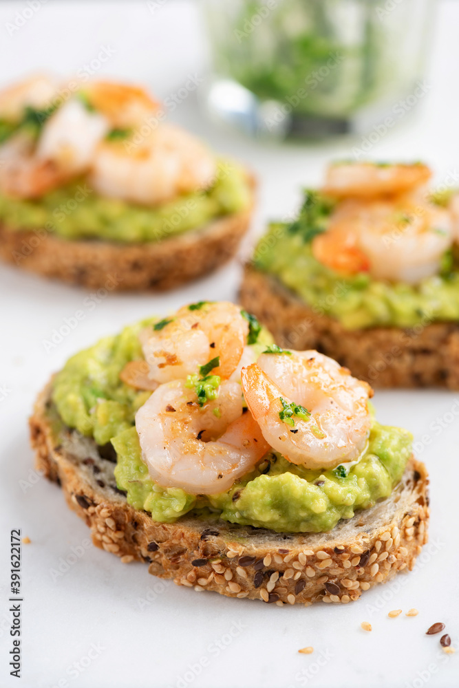 Bruschetta with avocado cream and shrimps on white marble background, closeup view. Appetizer or snack avocado toasts with prawn Bruschetta with avocado cream and shrimps on white marble background, closeup view. Appetizer or snack avocado toasts with prawn