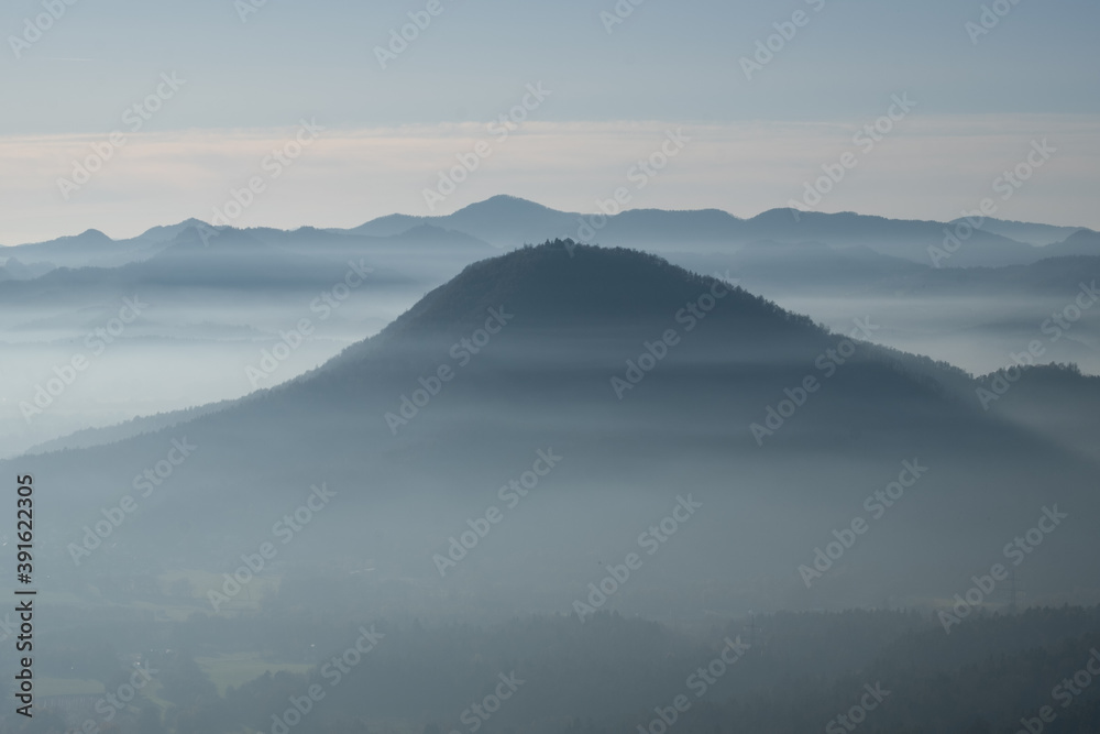 mystical and romantic mountain scenery with hilltops softly peaking out of white clouds. Fog flowing through the valleys. Layers of mountains in a beautiful landscape with the alps in the background 